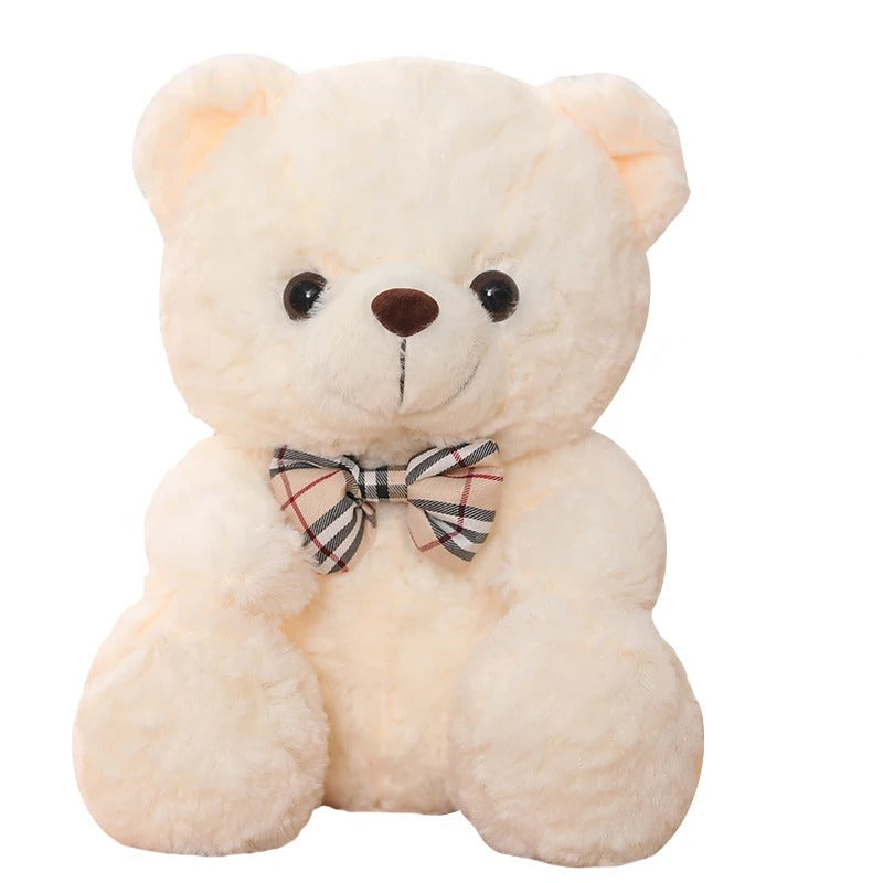 Un adorable ours en peluche crĂšme de 25cm avec un nĆud papillon Ă carreaux.