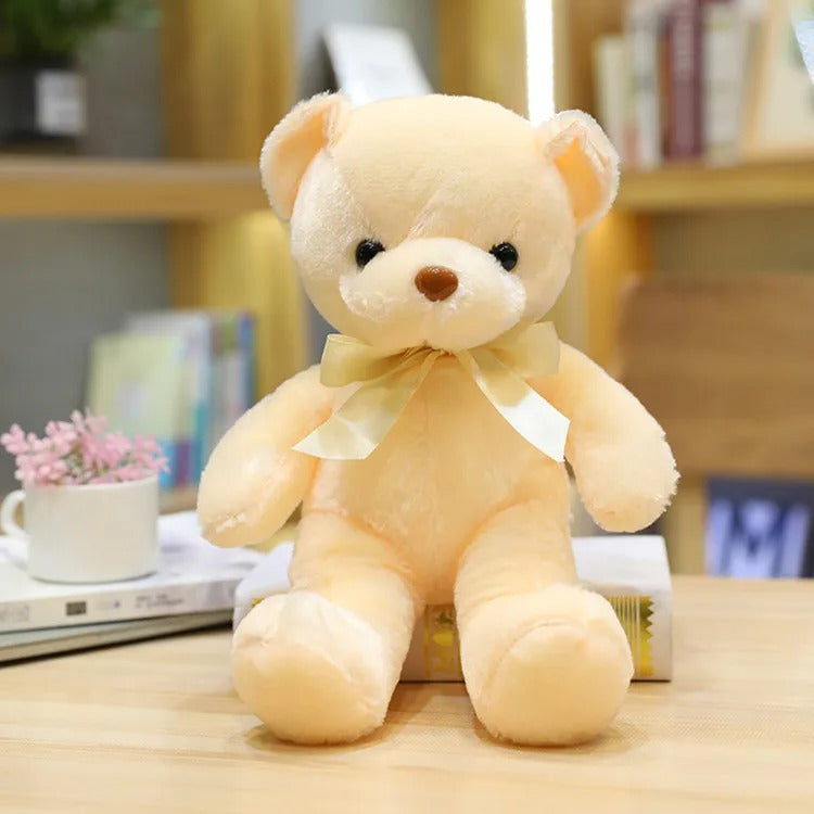 Charmant Ours en peluche beige avec un nĆud dorĂ©, assis, regardant adorablement.