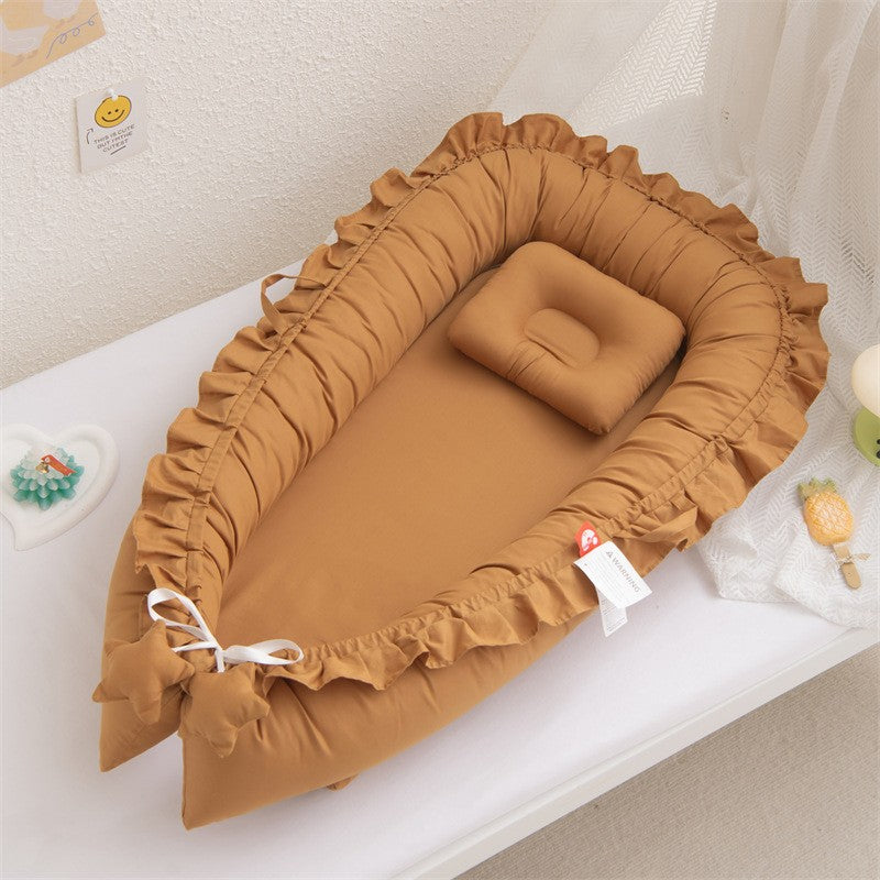 Un nid d'ange douillet pour bébé, de couleur camel avec des volants délicats sur les bords. Un petit oreiller rectangulaire assorti repose à l'intérieur, invitant au repos. Le nid est placé sur un fond blanc, suggérant un environnement sûr et confortable pour le nourrisson.