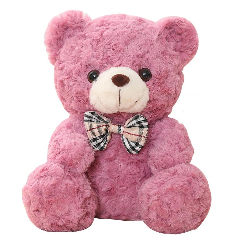 Adorable ours en peluche rose, doux et souriant, avec un nĆud papillon Ă©cossais.