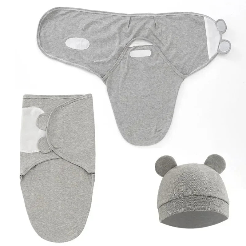 L'ensemble couverture d'emmaillotage Chaleur de Maman comprend trois pièces en coton gris : un lange avec détails de pattes blanches, une écharpe avec trous découpés et oreilles d'ours et un bonnet assorti avec deux oreilles d'ours rondes.