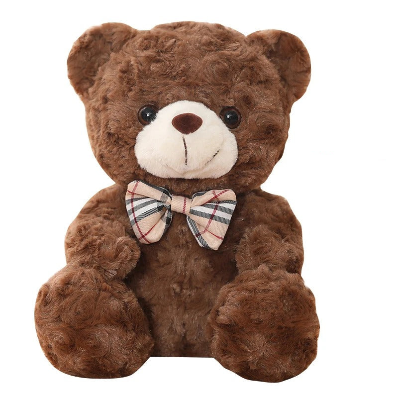 Un ours en peluche marron doux, souriant, avec un nĆud papillon Ă©cossais.