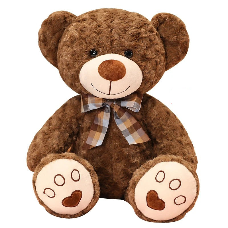 Un ours en peluche marron doux, souriant, avec un nĆud papillon Ă©cossais.