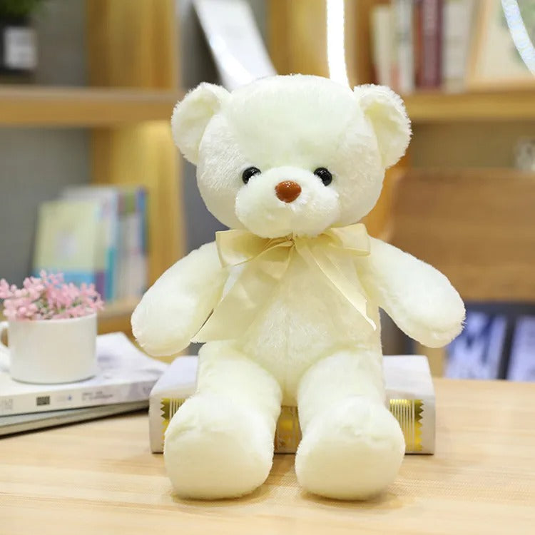 Un ours en peluche blanc crĂšme avec un ruban jaune pĂąle, assis.