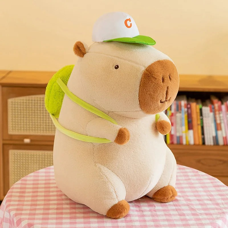 Peluche capybara adorable avec casquette et sac Ă dos vert.