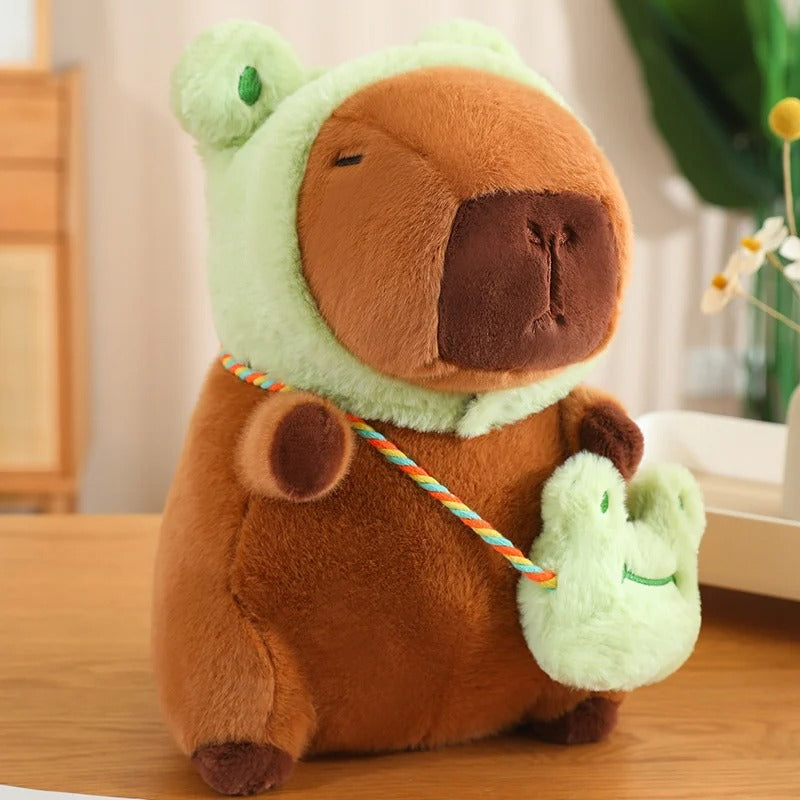 Peluche capybara adorable avec capuche grenouille verte, tenant une petite bourse.