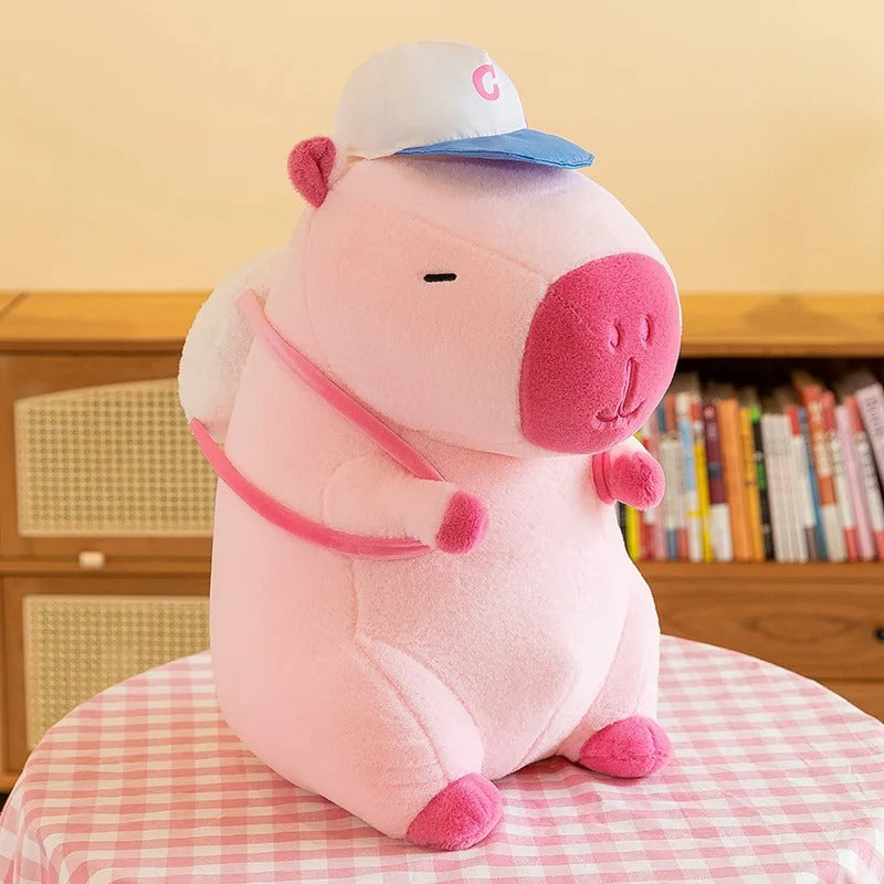 Peluche capybara rose, douce, portant casquette et sac Ă dos.
