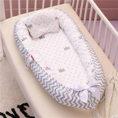 Le Réducteur de lit bébé | Nuit Douce, avec bordure grise et blanche à chevrons, tissus intérieurs couronnes et oreiller assortis, apporte confort et sécurité au sommeil de bébé grâce à son nœud blanc au bas.