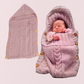 Un nouveau-né dort enveloppé dans une Couverture emmaillotage rose à boutons | Petit Rêve. À côté de lui, le lange est posé à plat, dévoilant sa capuche et ses boutons pour un sommeil paisible.