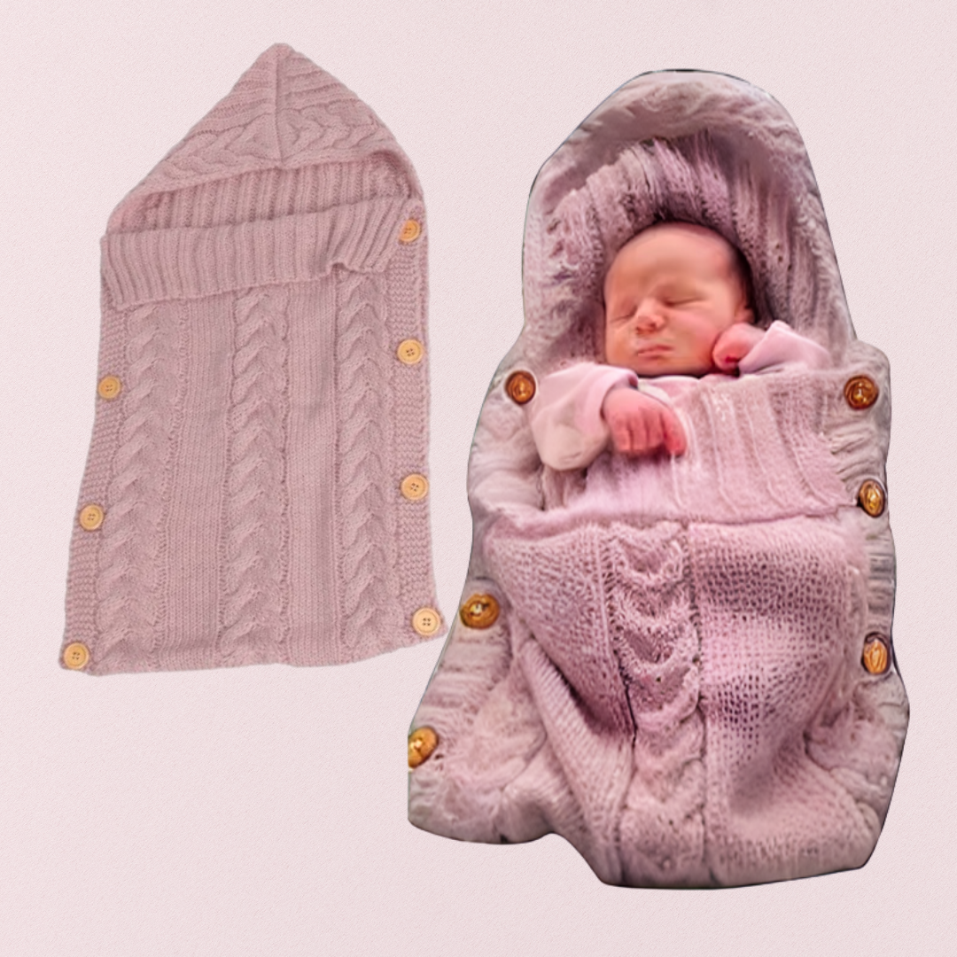 Un nouveau-né dort enveloppé dans une Couverture emmaillotage rose à boutons | Petit Rêve. À côté de lui, le lange est posé à plat, dévoilant sa capuche et ses boutons pour un sommeil paisible.