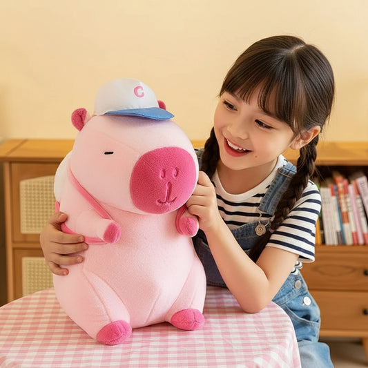 Fille souriante étreignant une peluche capybara rose avec une casquette.
