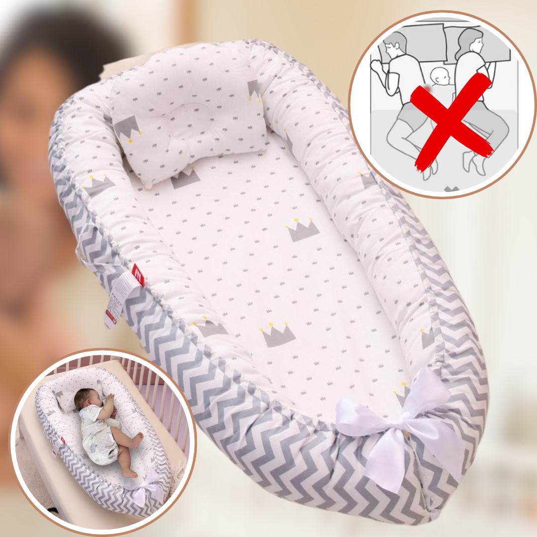Le Réducteur de lit bébé | Nuit Douce est un nid d'ange avec un petit oreiller, une bordure à chevrons gris et un motif couronne. Les inserts mettent en valeur un bébé profitant d'un sommeil paisible dans ce cocon rassurant et indiquent les dangers d'utilisation du berceau, indiqués par un X rouge.