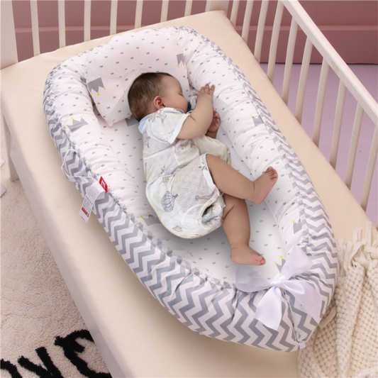 Un bébé dort en toute sécurité sur le côté dans le doux Nuit Douce Réducteur de lit bébé, orné d'un nœud blanc, bercé dans un berceau à barreaux blancs et un mur rose pâle en toile de fond.