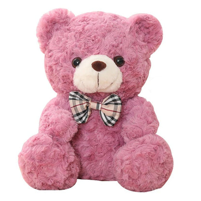 Adorable ours en peluche rose, doux et souriant, avec un nœud papillon écossais.