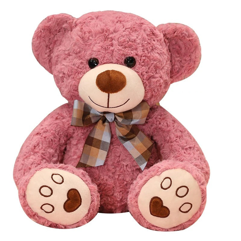 Adorable ours en peluche rose, doux et souriant, avec un nœud papillon écossais.
