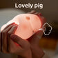 Gros plan des mains qui serrent un cochon en peluche Porcin™ doux et lumineux, suggérant une bouffée d'air avec une illustration de petit nuage. Les mots « Lovely pig » en haut soulignent son charme de veilleuse bébé.