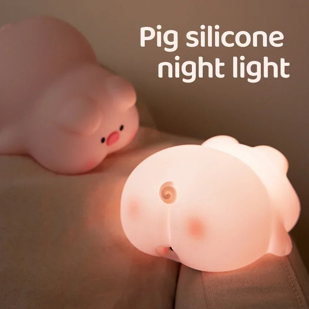 Une jolie veilleuse bébé Porcin™ repose doucement sur le lit, sa douce lumière brille doucement. Le design rond et cartoon du cochon présente une petite queue recourbée. Le texte « Veilleuse en silicone cochon » se trouve dans le coin supérieur droit.