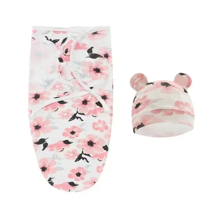 La couverture emmaillotage bébé Douce Câline™ à fleurs roses et blanches est accompagnée d'un bonnet à oreilles d'ours assorti, présenté sur un fond blanc, idéal pour apaiser le réflexe de Moro et assurer un sommeil paisible.