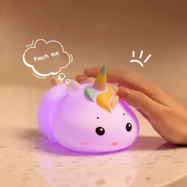 Une main effleure doucement la veilleuse bébé licorne lumineuse UniGlow™ sur le comptoir. Sa crinière colorée et son petit visage émettent une douce lumière violette. Une bulle de pensée dit « Pincez-moi ! » avec un petit point d'exclamation, promettant des nuits paisibles à venir.