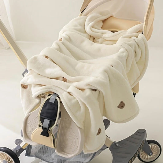 Une poussette beige recouverte d'une douce Couverture bébé | P'tit Câlin™. Avec ses petits visages d'ours bruns et ses plis douillets, cette couverture multifonctionnelle garde votre tout-petit bien au chaud.