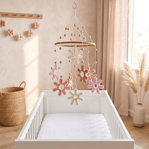 Mobile bébé fleurs pastel en macramé suspendu au-dessus d'un lit bébé dans une chambre bohème rose et crème