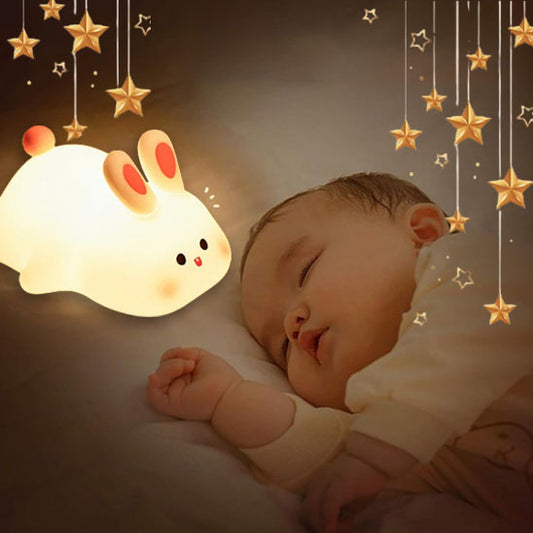 Un bébé endormi repose sur son lit, entouré détoiles lumineuses. La veilleuse lapin BunnyGlow™ de Petitsbeautes illumine doucement la nuit, servant de compagnon doux et créant une ambiance paisible.