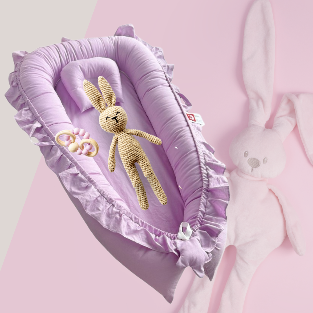 Douceur et sécurité pour bébé :** Un lit bébé portable mauve clair avec oreiller et détails à volants, placé dans un berceau, offrant un environnement de sommeil confortable et protégé.