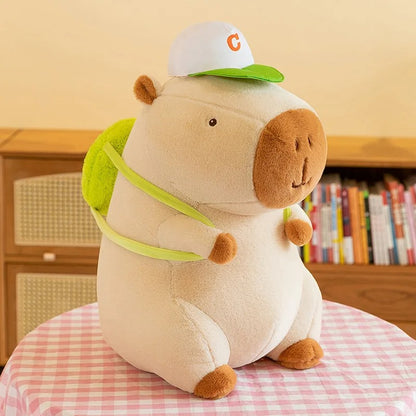 Peluche capybara adorable avec casquette et sac à dos vert.
